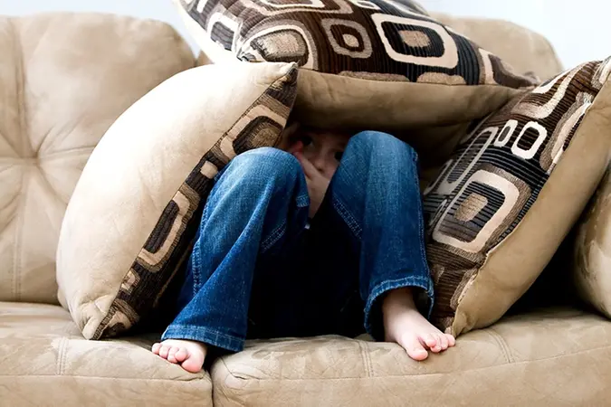 Bild på en pojke som gömmer sig under soffkuddar