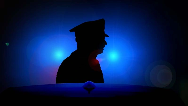Silhuetten av en man med polismössa i mörkret.