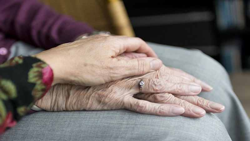 En yngre persons hand som vilar över en äldre persons händer.